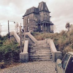 a car parked in front of a large house on the side of a hill with stairs leading up to it