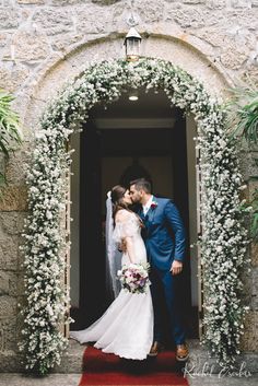 a bride and groom kissing in front of an archway with flowers on it at their wedding