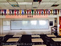 an empty classroom with desks and chalkboards hanging from the ceiling in front of a whiteboard