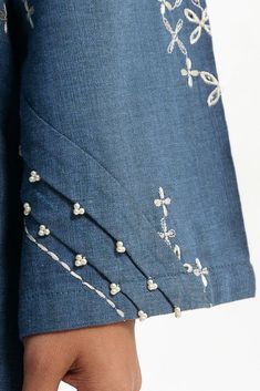 a woman's hand with beaded designs on her blue shirt and jeans jacket