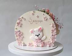 a white cake decorated with pink flowers and a teddy bear on it's side