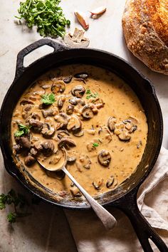 a skillet filled with mushroom soup on top of a table next to bread and parsley