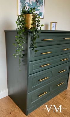 a green dresser with gold handles and brass knobs on the top, has a plant growing out of it