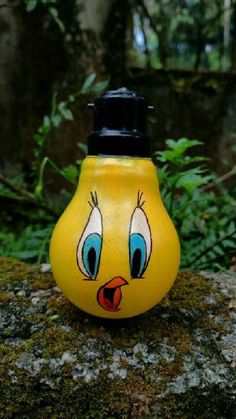 a yellow light bulb with eyes painted on it sitting on a mossy rock in the woods