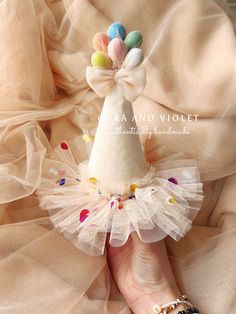 a woman's hand is holding a small white ballerina doll with multicolored balloons on it