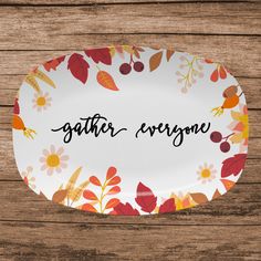 a plate with the words gather everyone written on it and colorful leaves around it, sitting on a wooden surface