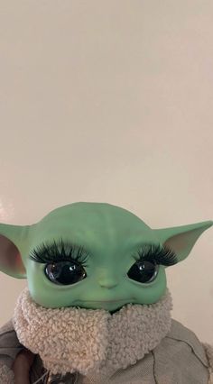 the child yoda doll has long eyelashes and is wearing a white coat with a fur collar