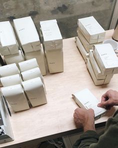 a man sitting at a table with many boxes on top of it and writing in a notebook