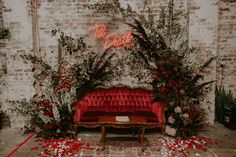 a red couch sitting in front of a brick wall with greenery and flowers on it