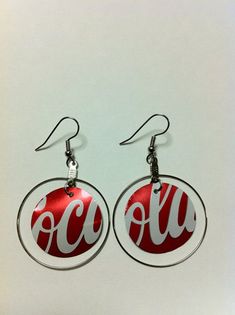 coca cola earrings are hanging from silver earwires with red and white letters on them