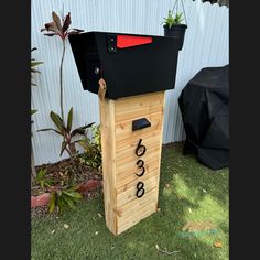 a mailbox sitting in the grass next to a fence with plants growing out of it