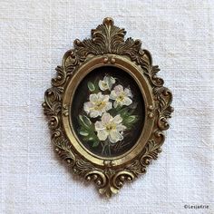 an ornate gold frame with flowers painted on the inside is hanging on a white fabric