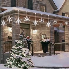 a snow covered christmas tree in front of a house with lights hanging from it's roof