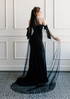 a woman in a black dress is standing with her back to the camera and wearing a veil