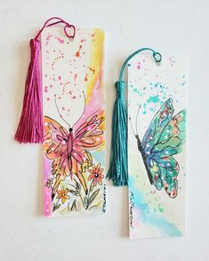 two cards with tassels on them and one has a butterfly painted on it