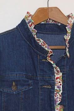 an old jean jacket is hanging on a wooden hanger with a flowered tie