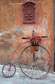 an old bicycle with flowers in the basket is parked next to a wall and door