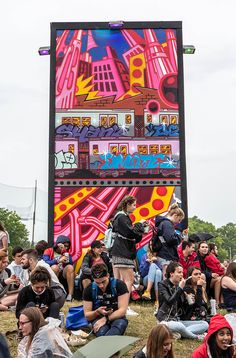 a group of people sitting on the ground in front of a large sign with graffiti