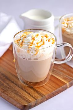 two glasses of hot chocolate with whipped cream and caramel sprinkles on a wooden tray