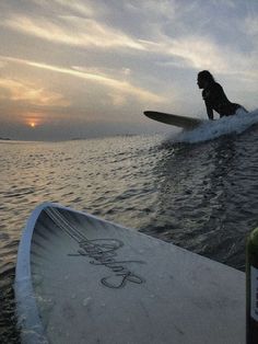 a person riding a surfboard on top of a body of water in the sunset