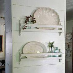 two white shelves with plates and vases on them against the wall in a dining room