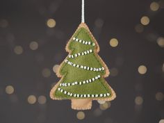 a felt christmas tree ornament hanging from a string with lights in the background