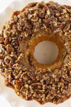 a close up of a doughnut on a white plate with pecans around it