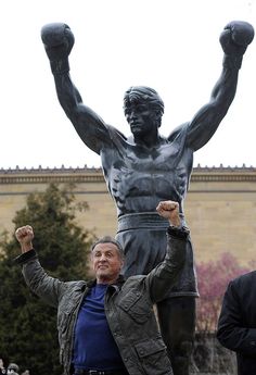 a man standing in front of a statue with his arms up and two fists raised