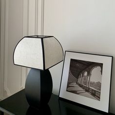 a lamp sitting on top of a black table next to a framed photo and an empty picture