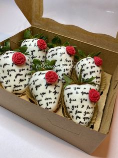 six decorated strawberries in a box with red roses on the top and white frosting