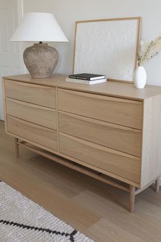 a wooden dresser with a lamp on top of it next to a white rug and door