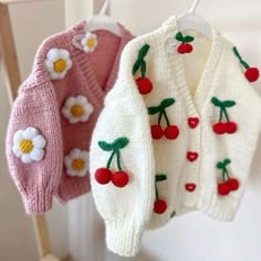 three knitted cherry sweaters hanging from hooks