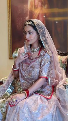 a woman sitting on top of a couch wearing a wedding dress and veil with her finger in her mouth