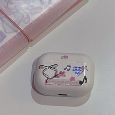 an apple airpods sitting on top of a table next to a pink case with musical notes