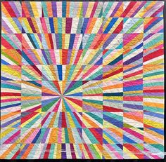 a multicolored quilt is displayed in front of a gray background with an image of a sunburst that appears to be made out of many different colors