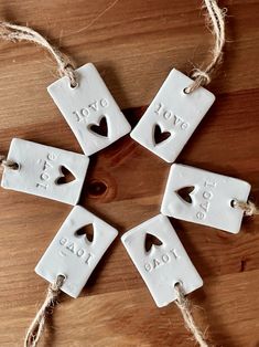 four white ceramic ornaments with words on them hanging from twine strings and jumbo rope