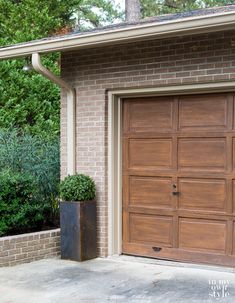 a large wooden garage door in front of a brick building with a planter next to it