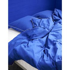 an unmade bed with blue sheets and pillows on top of it, next to a wall