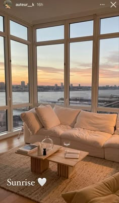 a living room filled with furniture and large windows overlooking the water at sunset or sunrise