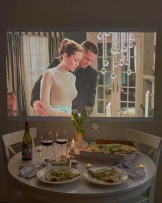 a man and woman standing in front of a tv screen with food on the table