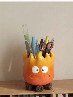 an orange container with pens, scissors and pencils in it sitting on a shelf