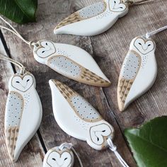 four white ceramic owl ornaments hanging from strings on a wooden table next to green leaves