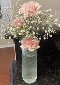 a vase filled with pink and white flowers on top of a black marble countertop