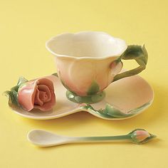 a tea cup and saucer with a rose on the side sitting on a yellow surface