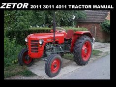 an old red tractor is parked on the side of the road in front of some bushes