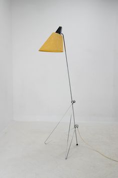 a floor lamp with a yellow shade on the base and a white wall behind it