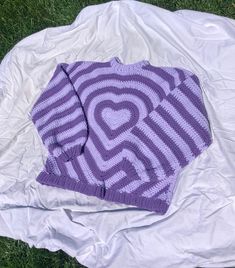 a purple knitted sweater laying on top of a white plastic bag in the grass