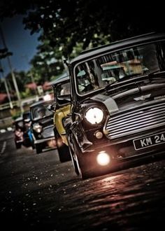 an old fashioned car is driving down the street at night with its headlights turned on