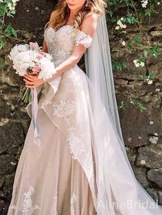 a woman in a wedding dress standing next to a stone wall with flowers on it