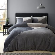 a bed with grey sheets and pillows in a room